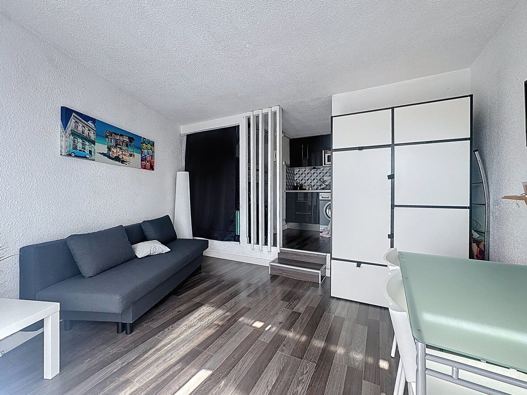 A compact living space with a sofa, a dining table, a kitchenette, and a door leading to a laundry area.