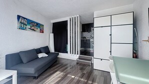 Een knus woongedeelte met een bank, een eettafel, een kitchenette en een deur naar een wasruimte.