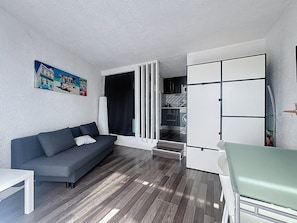 A compact living space with a sofa, a dining table, a kitchenette, and a door leading to a laundry area. - Le Port Carnon, Parenthèse Marine (Carnon-Plage)