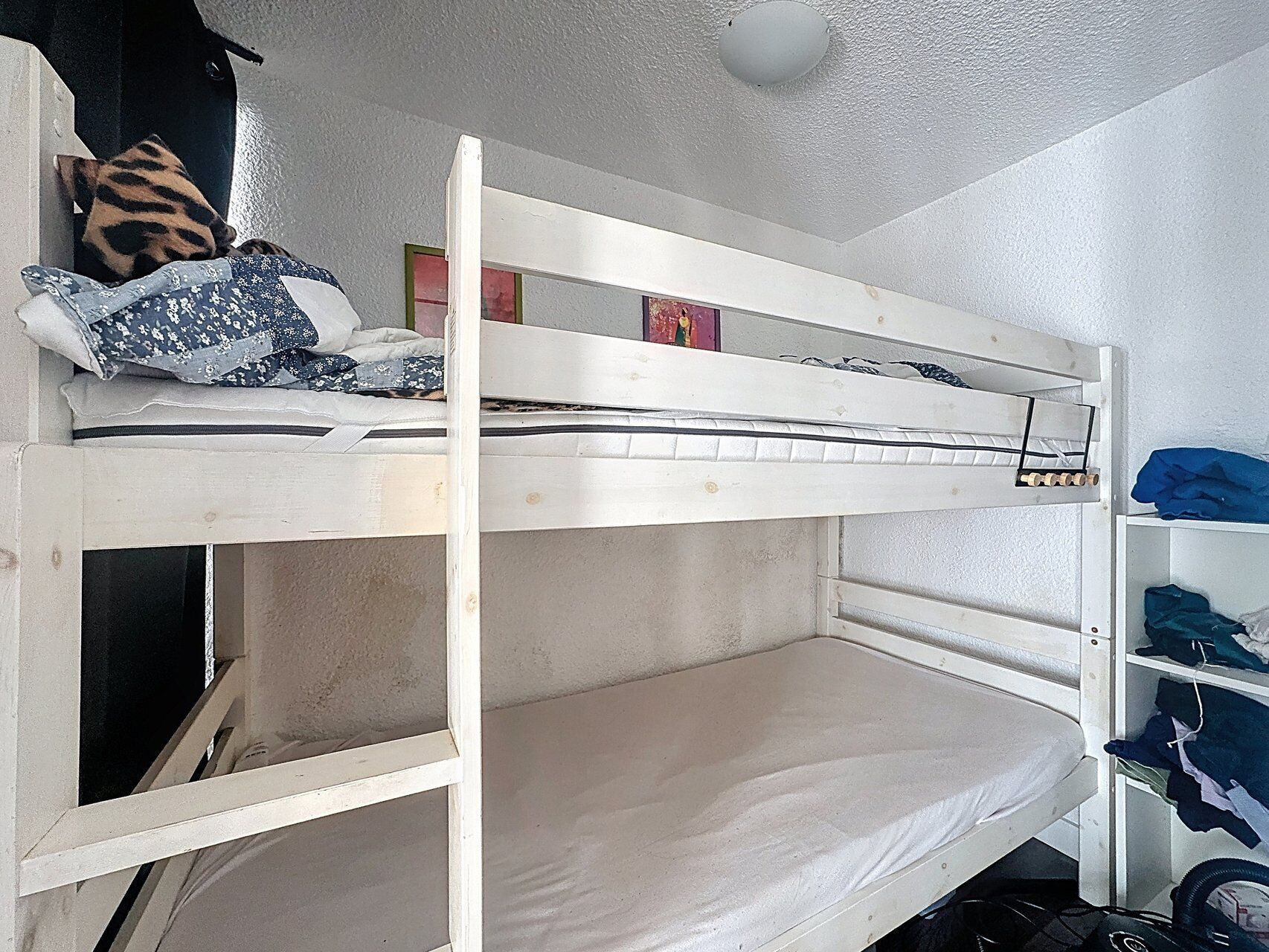 A bunk bed with a lower bunk, a pillow, and a shelf with folded clothes.