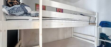 A bunk bed with a lower bunk, a pillow, and a shelf with folded clothes.