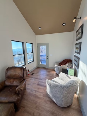 A spacious room with a large window, a door, and a seating area with a brown leather chair and a patterned armchair.
