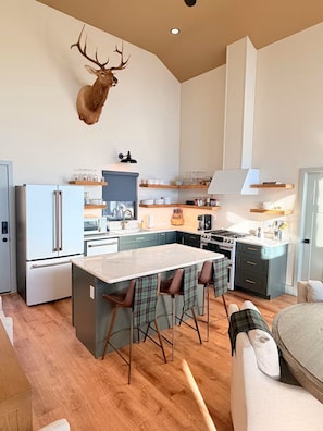 A modern kitchen with a central island, a mounted deer head, and a dining area with plaid chairs.