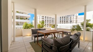 A rooftop terrace with a wooden table and chairs, a sofa, and a view of surrounding buildings. - L'apogée, centre et terrasse (Montpellier)