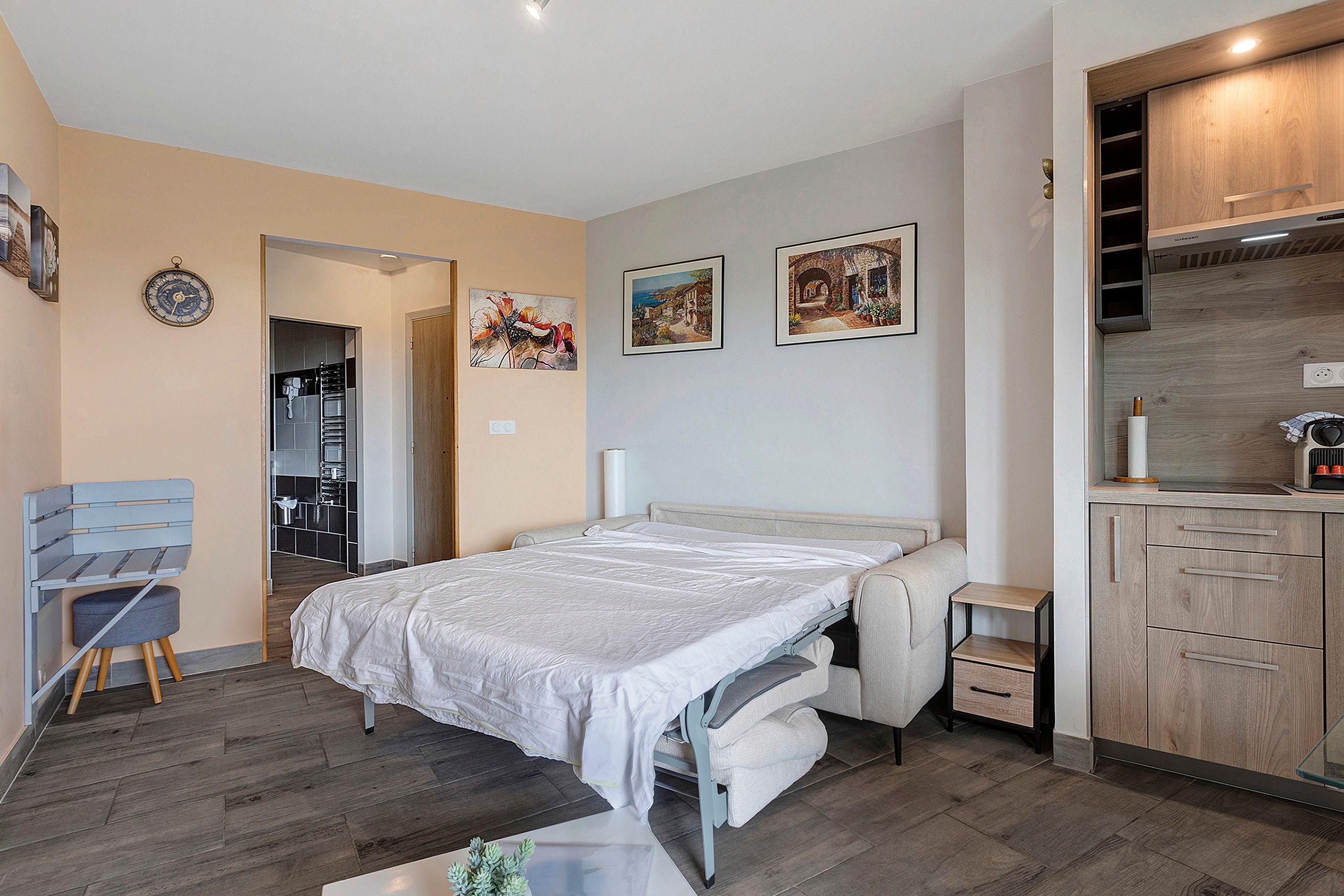 Ein modernes Schlafzimmer mit einem Bett, einem Sessel, einem kleinen Tisch und einer Küchenzeile.