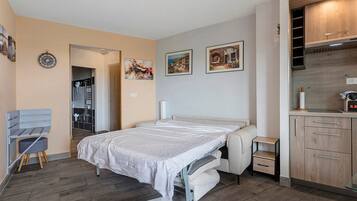 Ein modernes Schlafzimmer mit einem Bett, einem Sessel, einem kleinen Tisch und einer Küchenzeile.