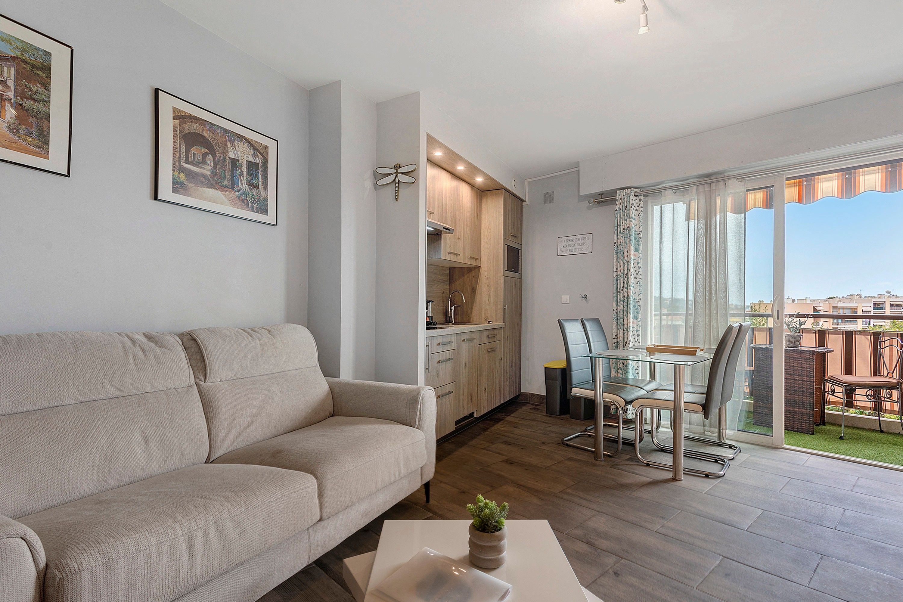 Una sala de estar con sofá, una mesa de comedor con sillas, una zona de cocina y un balcón con vistas.