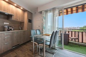 A modern kitchen with wooden cabinets, a built-in microwave, and a dining area with a glass table and chairs. - Le Beauséjour, Studio with Rooftop Pool (Le Cannet)
