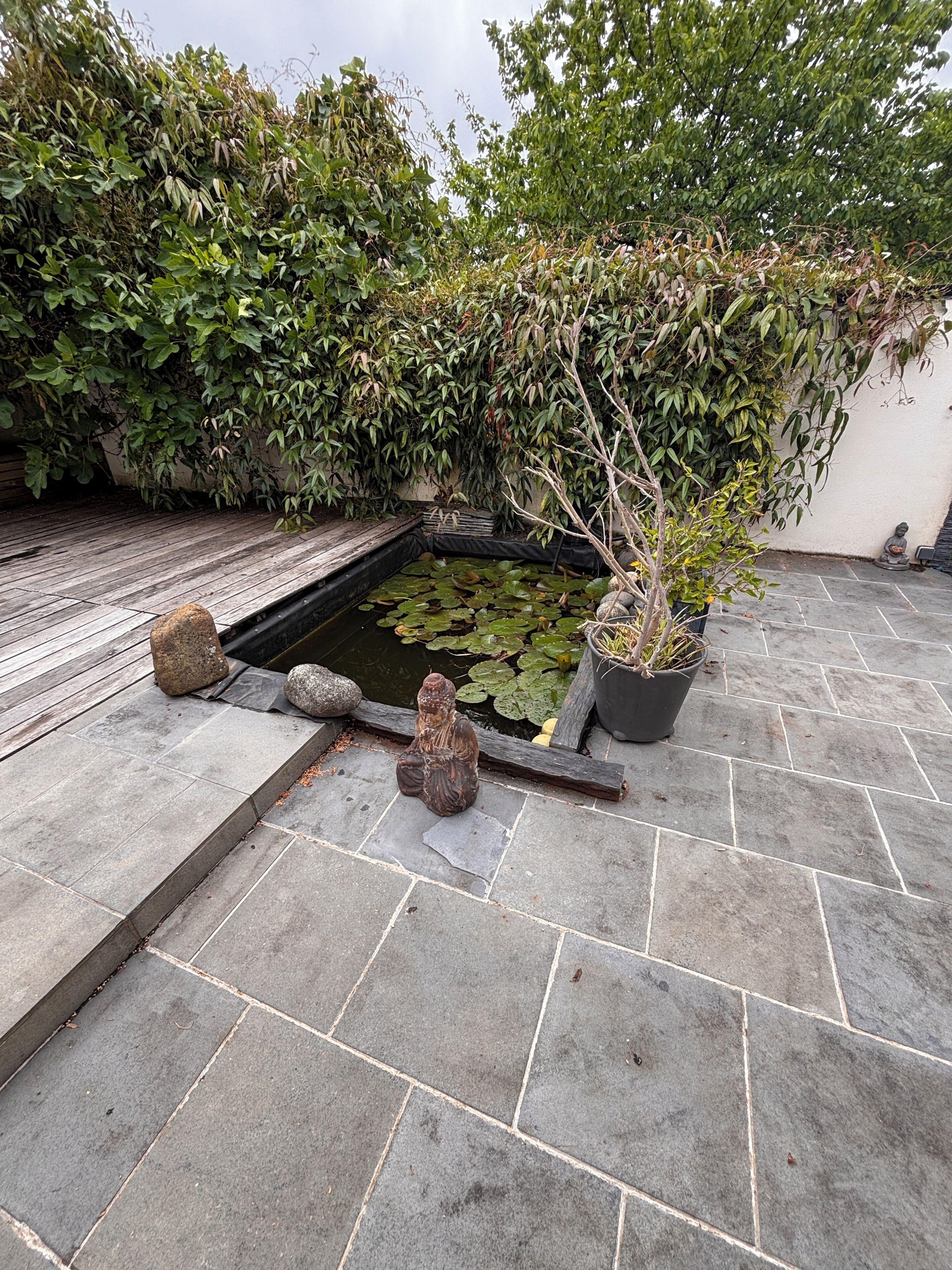 A koi pond with a statue, surrounded by stone tiles and lush greenery.