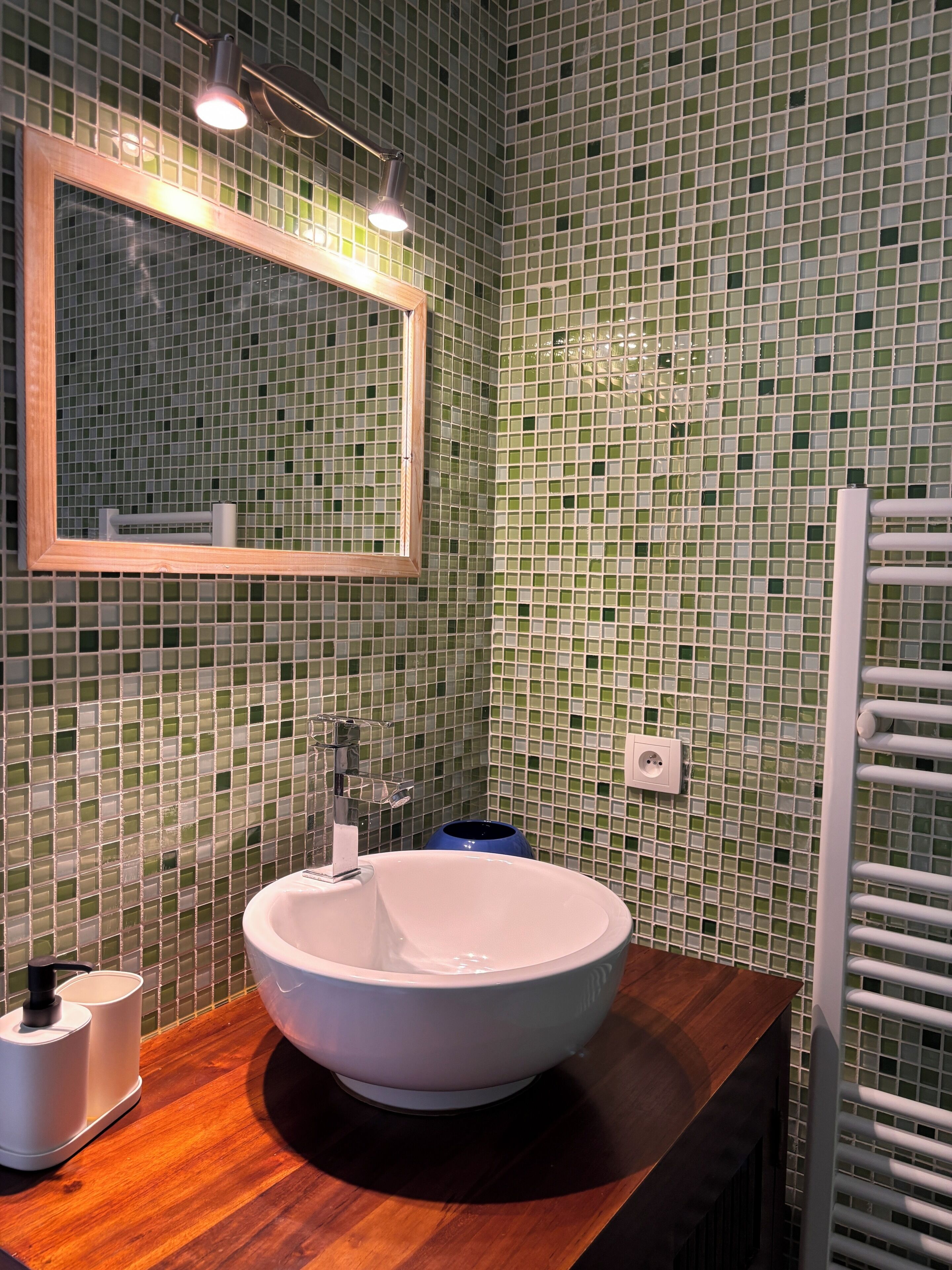 A bathroom with a round sink, a mirror, and green mosaic tiles.