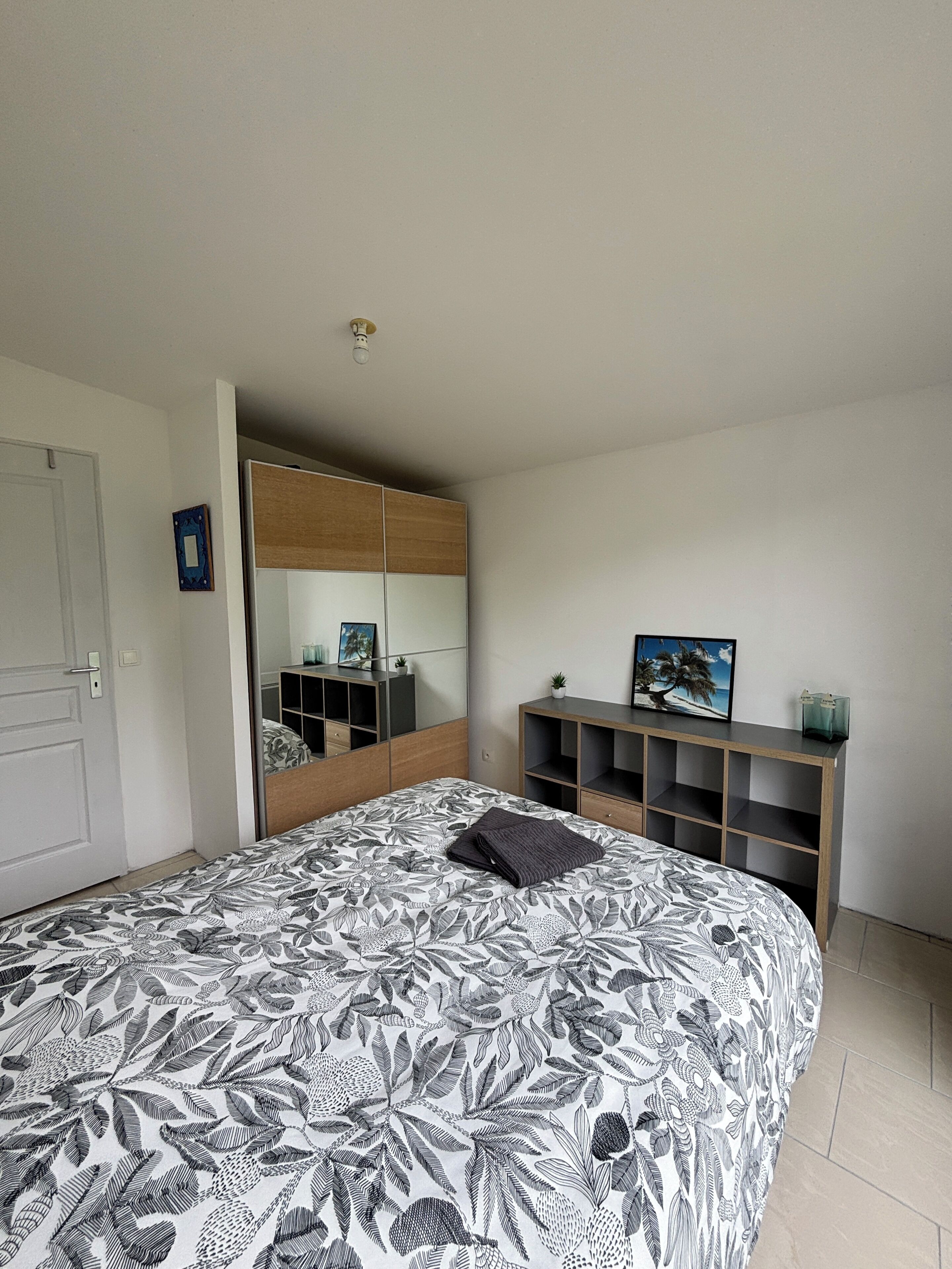 A bedroom with a bed, a wardrobe, a mirror, and a shelf with decorative items.