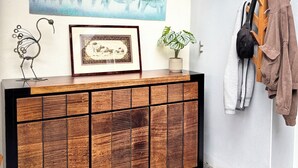 A modern interior with a wooden cabinet, a framed picture, a zebra painting, a plant, and a coat rack with clothes. - The Elephant House in Vivonne (Vivonne)