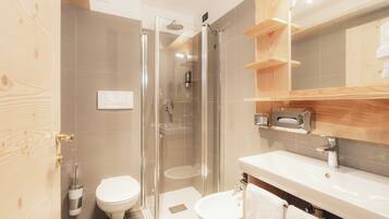 Un baño moderno con ducha de vidrio, inodoro blanco, lavamanos y estantes de madera.