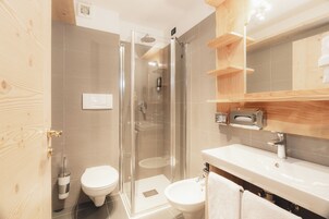Un baño moderno con ducha de vidrio, inodoro blanco, lavamanos y estantes de madera.