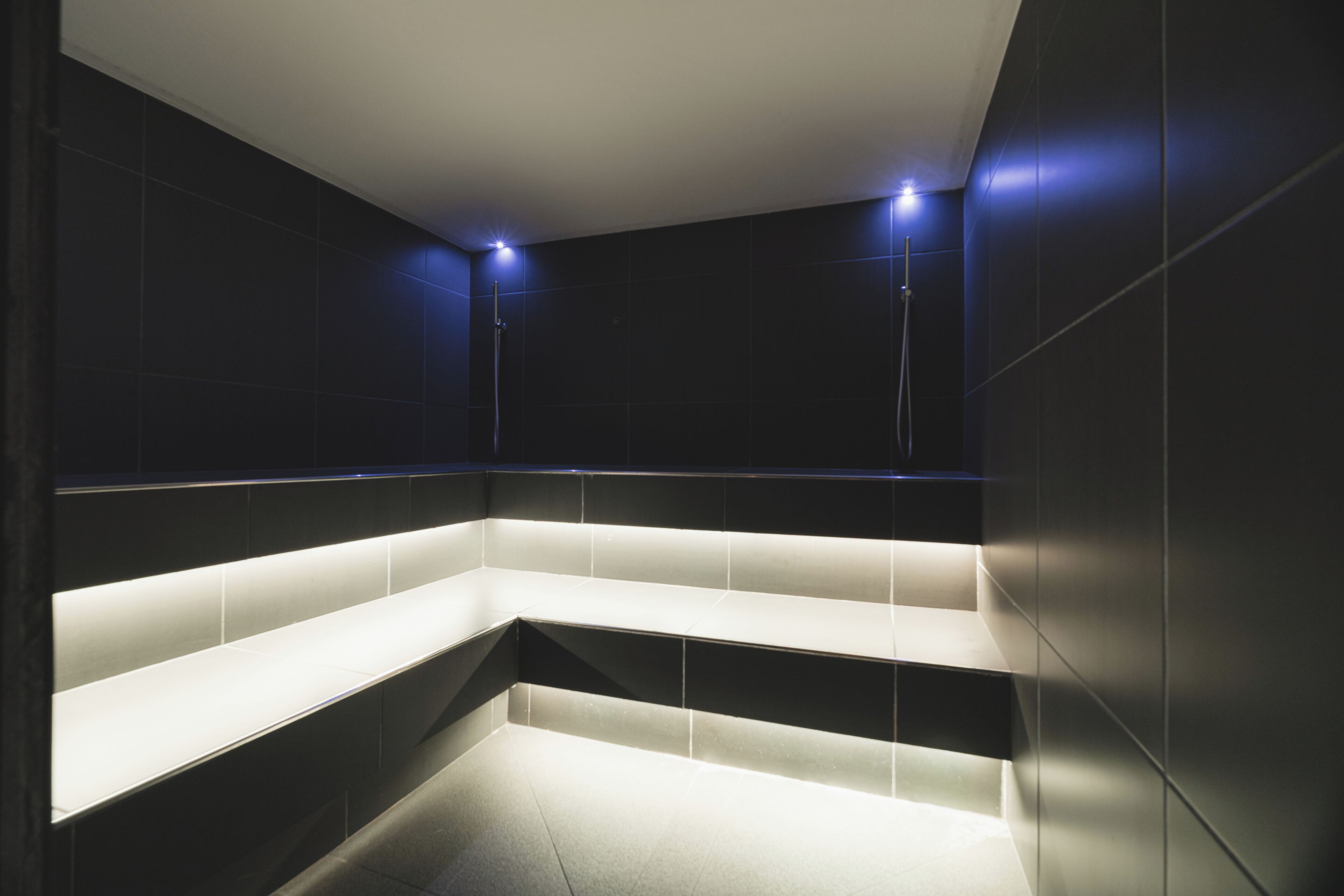 A modern bathroom with dark tiles, a built-in bench, and recessed lighting.