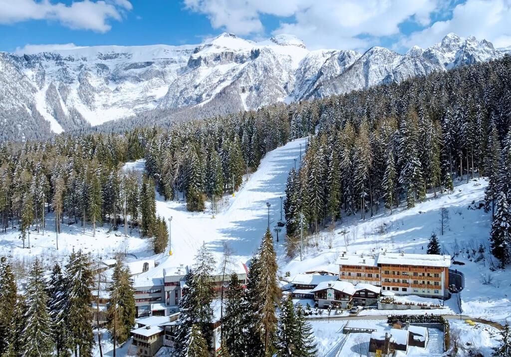 A snow-covered mountain resort with a ski slope, lodge, and forested area.