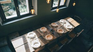 Mesa de comedor dispuesta con platos, vasos y cubiertos, con bombillas colgantes arriba.