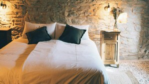 Un dormitorio con pared de piedra, una cama con ropa blanca, dos lámparas de noche y una mesita de noche de madera con un jarrón.