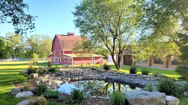A red barn, a pond with rocks, and a well-maintained lawn.