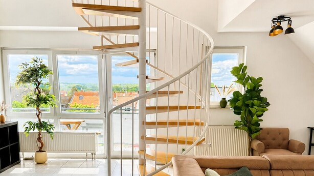 A modern living room with a spiral staircase, a brown sofa, and a view of the outside. - Velmora Boutique Suites Rheingau - Balcony & Grill (Oestrich-Winkel)