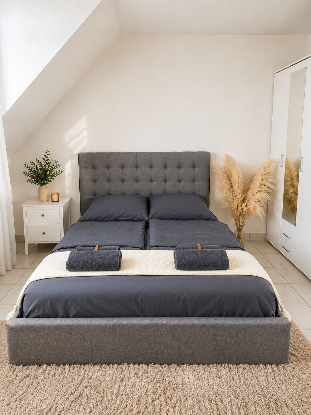 Een moderne slaapkamer met een groot bed, een nachtkastje met een plant en een kledingkast.