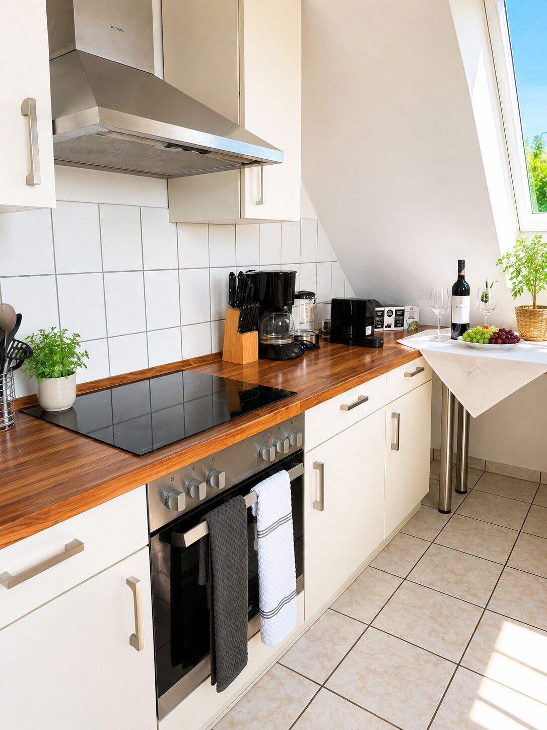 A modern kitchen with a black induction cooktop, stainless steel appliances, and a window providing natural light.
