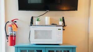 Un meuble de couleur turquoise avec un four à micro-ondes posé dessus, un extincteur accroché au mur et un téléviseur fixé au-dessus.