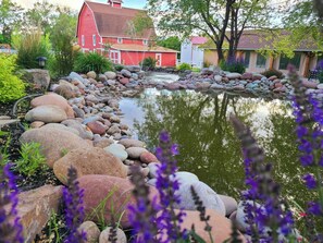 A pond with surrounding rocks and purple flowers, a red barn, and a house with a red roof. - Romantic Rustic Luxury on 21-acre Private Ranch #5 (Silt)