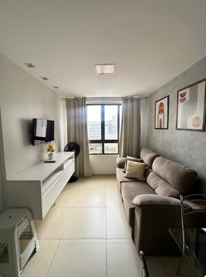 Ein Wohnzimmer mit einer Couch, einem Fernseher und einem Fenster mit Vorhängen.