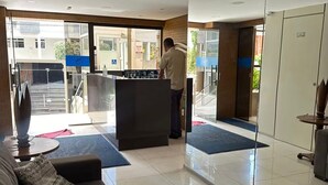 Um saguão de hotel com uma mesa de recepção, um sofá e uma janela grande.