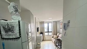 Um corredor estreito que dá para uma cozinha e uma sala de estar, com geladeira, uma mesinha e um sofá.