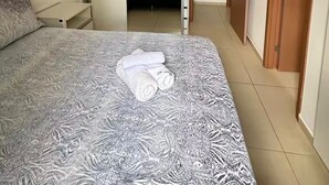 Quarto com cama, guarda-roupa e banheiro visível por uma porta aberta.