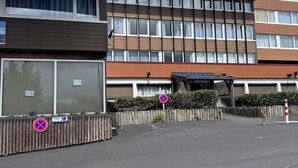 Un edificio de varios pisos con zona de estacionamiento, un cartel de prohibido estacionar y un letrero de accesibilidad para sillas de ruedas.