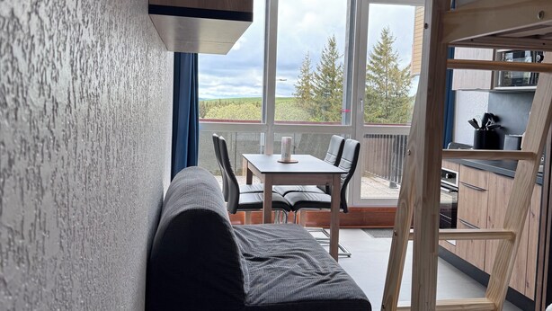 Una habitación moderna con literas, un pequeño sofá, una mesa de comedor con sillas y vistas al exterior.