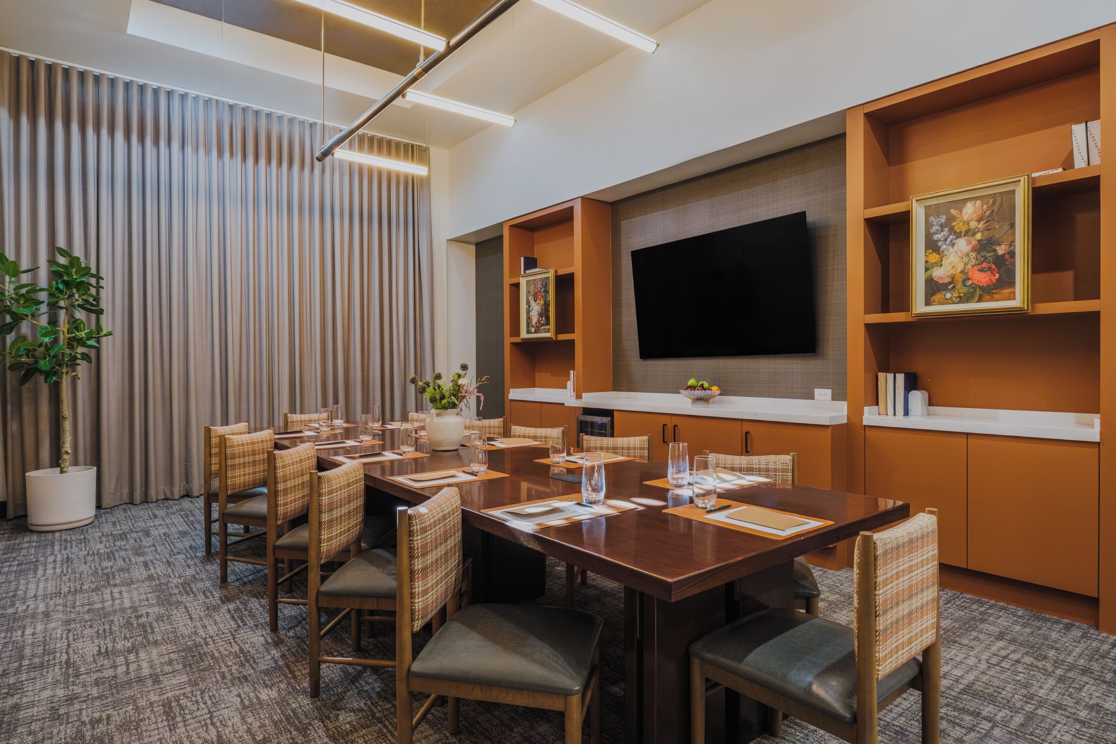 A conference room with a large table, chairs, a flat-screen TV, and a bookshelf.