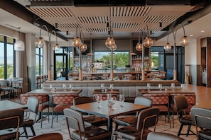 Un restaurante con zona de bar, diferentes disposiciones de asientos y vistas al exterior.