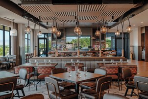 Un restaurante con zona de bar, diferentes disposiciones de asientos y vistas al exterior.