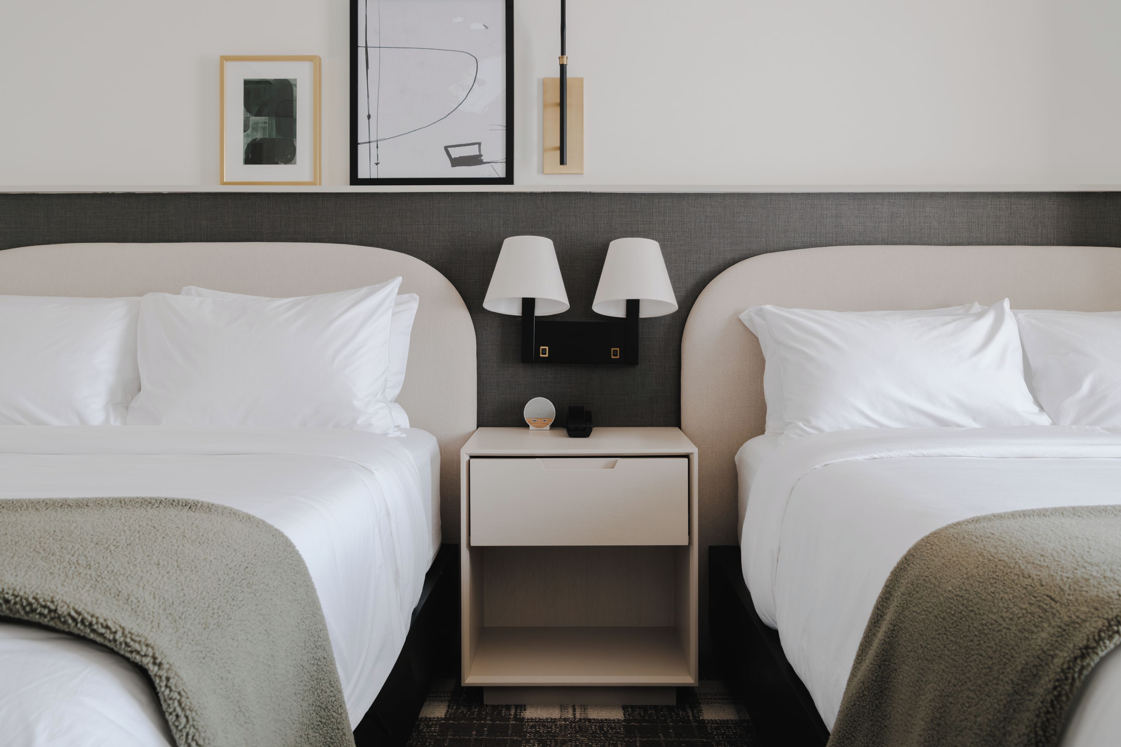Une chambre d’hôtel avec deux lits, une table de chevet avec une lampe et un tableau accroché au mur.