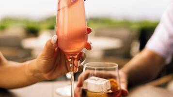 Una mesa de madera con un vaso de bebida rosa y una botella de whisky.