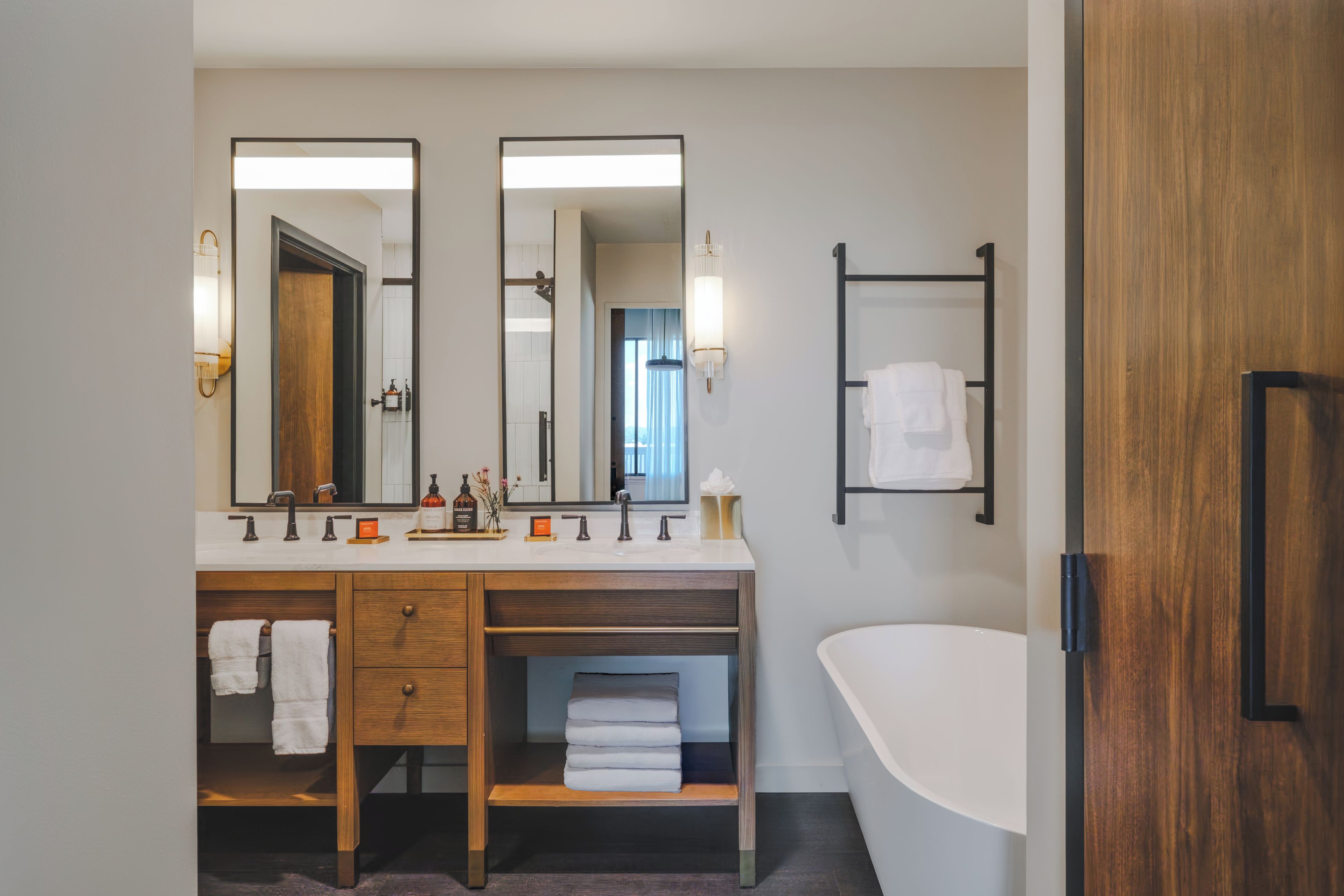 Une salle de bain moderne avec un meuble-lavabo en bois, un grand miroir, une baignoire sur pieds et un porte-serviettes.