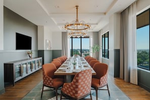 Une salle à manger avec une longue table dressée pour un repas, entourée de chaises, et un lustre moderne au-dessus.