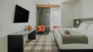A hotel room with a bed, a desk, a chair, a TV, and a window with curtains.