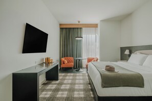 A hotel room with a bed, a desk, a chair, a TV, and a window with curtains. - Hotel Longmont (Longmont)