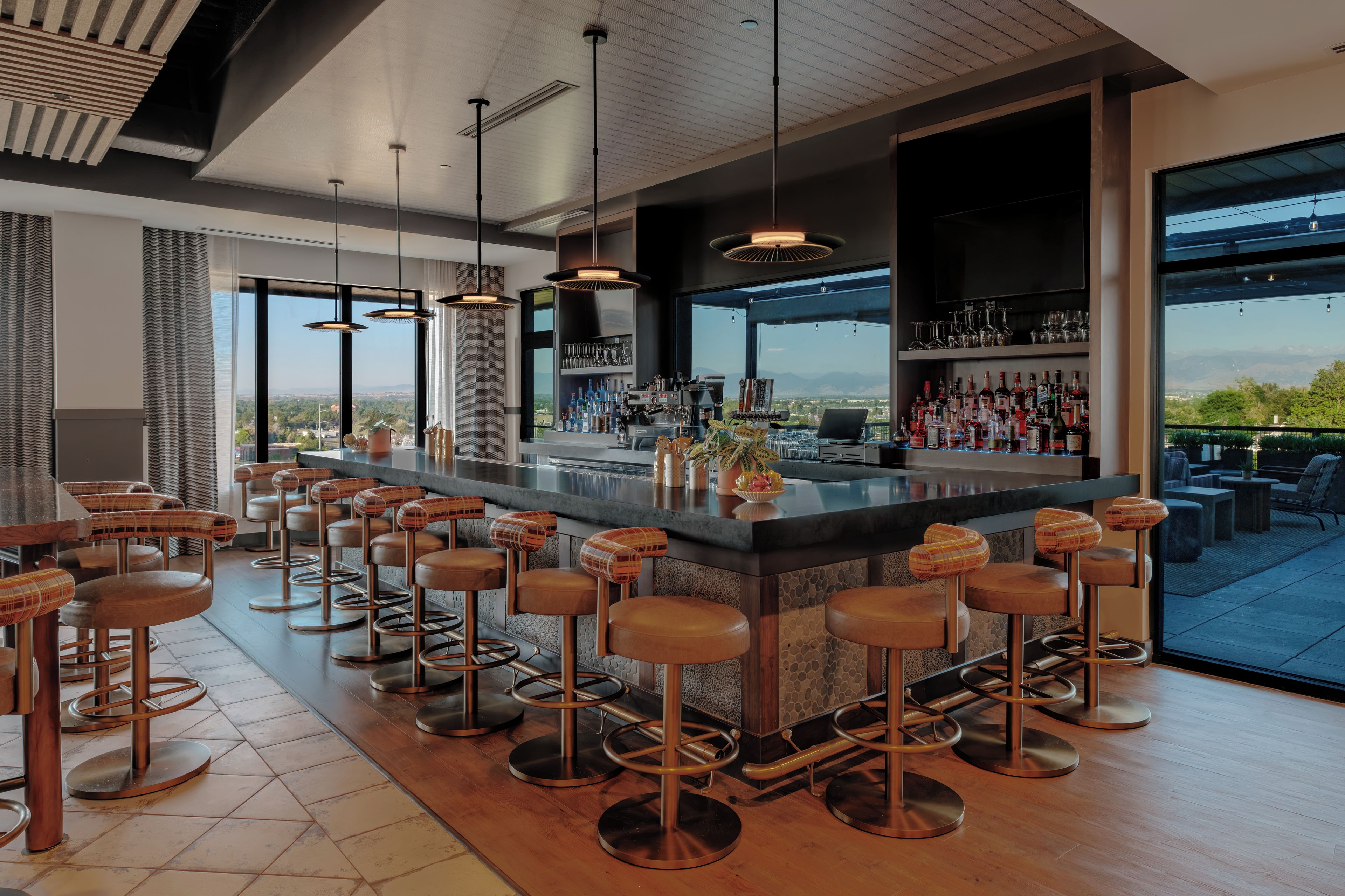 A modern bar area with multiple stools, a bar counter, and a view of the outdoors.