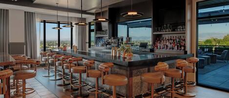 A modern bar area with multiple stools, a bar counter, and a view of the outdoors.