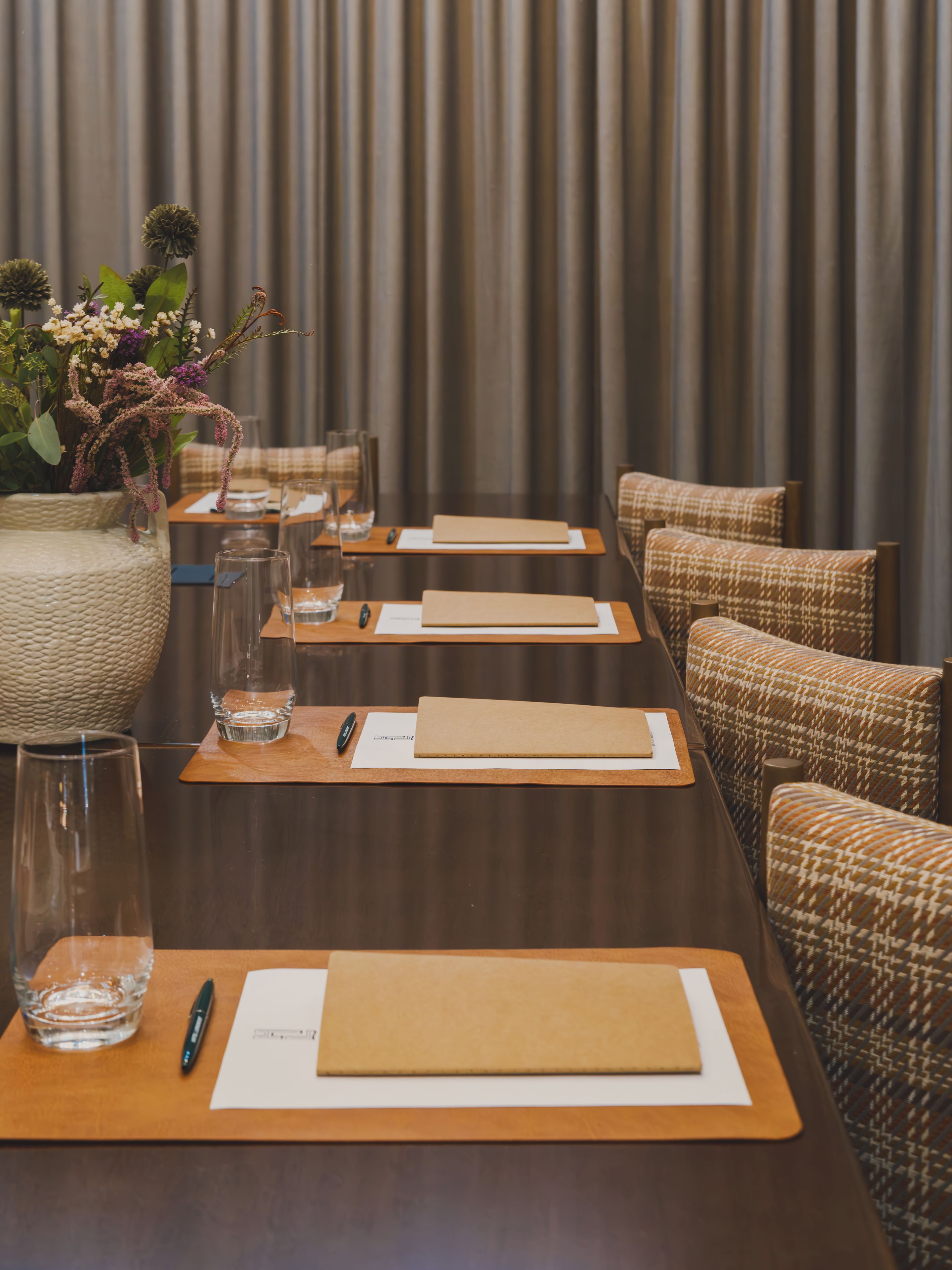 Un salón de conferencias con una larga mesa, sillas y un jarrón decorativo con flores.