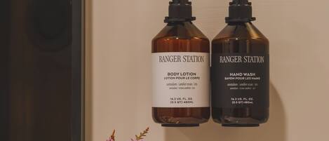 A bathroom with two bottles of Ranger Station body lotion and hand wash on a shelf, a vase with flowers, and a white towel.