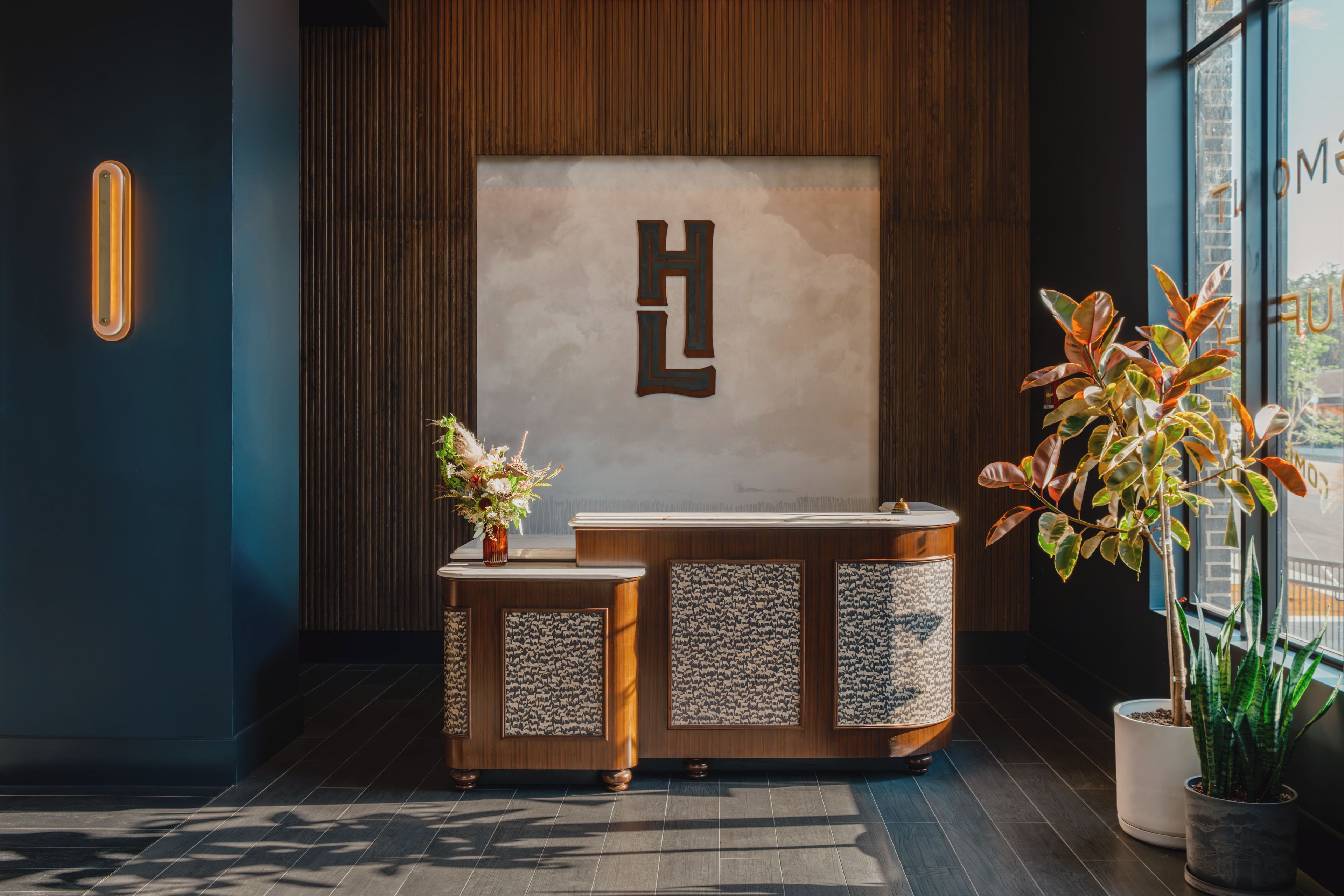 En receptionsdisk med modern design, ett stort "EL" på väggen och en krukväxt till höger.