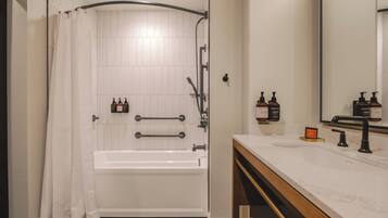 A bathroom with a bathtub, a shower, a vanity with a mirror, and toiletries.