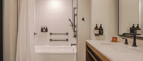 A bathroom with a bathtub, a shower, a vanity with a mirror, and toiletries.